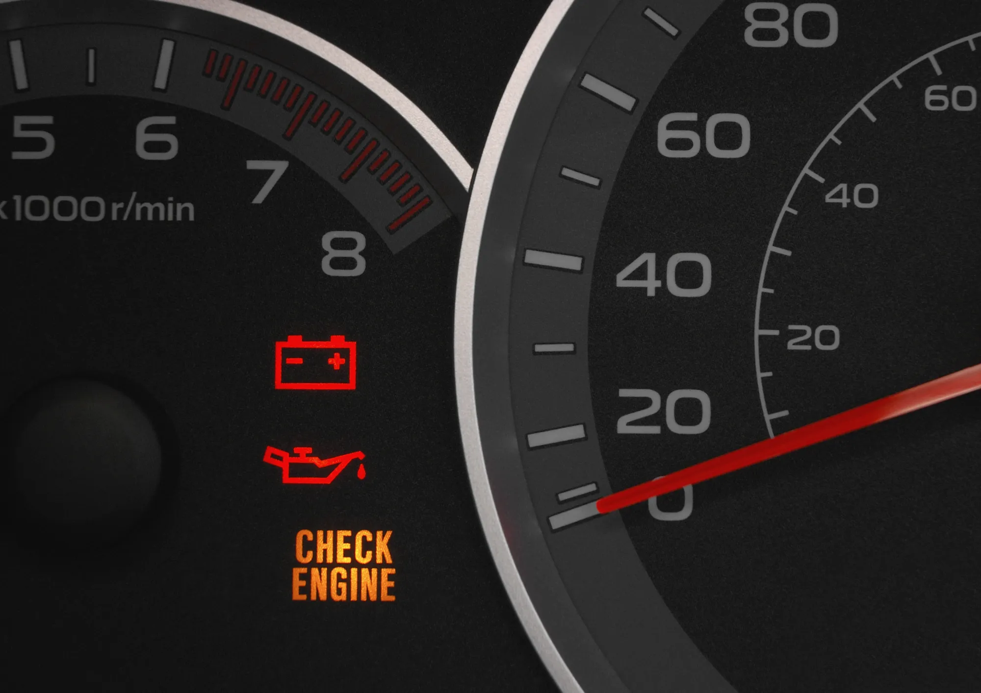 Close-up of a car dashboard with lit red battery and oil warning lights and an amber check engine light beside the tachometer and speedometer.
