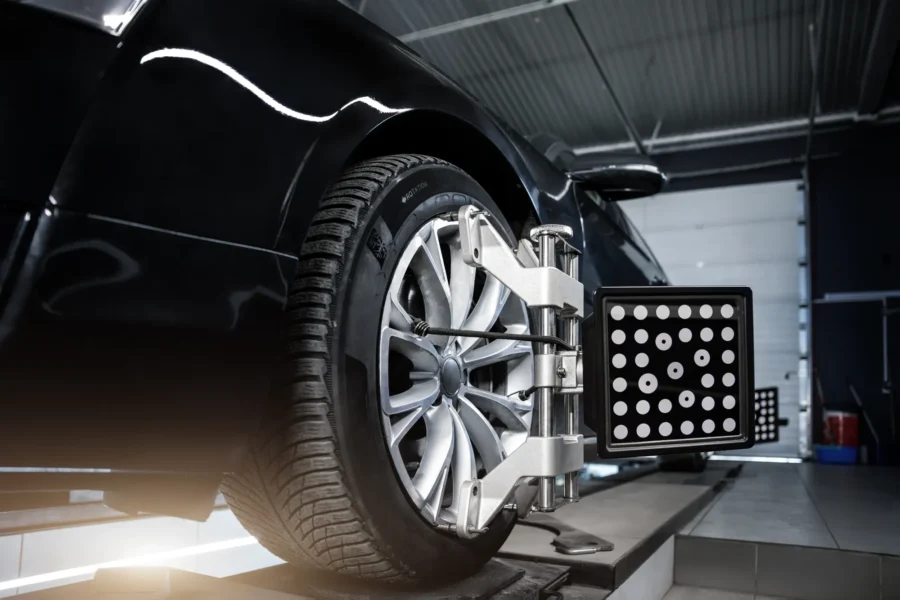 A wheel alignment target board clamped to the alloy wheel of a black car on an alignment rack in a repair shop.